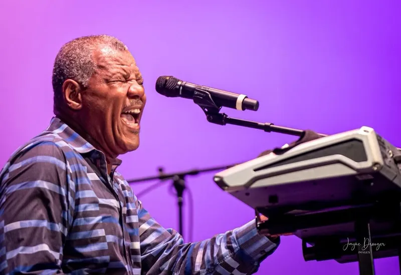 Shawn Brown sings with eyes closed at his keyboard and microphone against a vivid purple stage backdrop