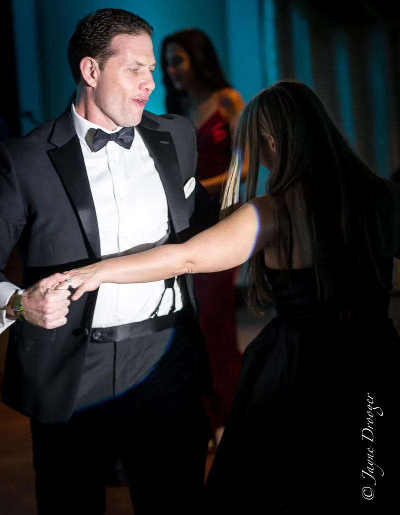 A man in a tuxedo and bow tie dances with a long-haired woman in a black dress