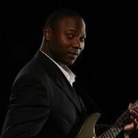 Reggie A. Ward in a black suit holding an electric guitar